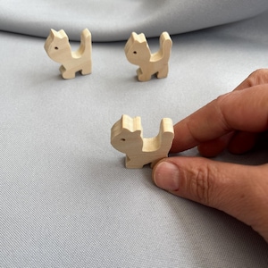 May include: Three wooden cat figurines, each with a simple, cartoon-like design. The cats are light brown and have a slightly distressed finish.