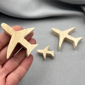 Könnte beinhalten: Drei Holzspielzeugflugzeuge in verschiedenen Größen. Die Flugzeuge sind aus hellem Holz gefertigt und haben ein schlichtes Design. Die Flügel und das Heck sind klar definiert, und die Gesamtästhetik ist sauber und minimalistisch.