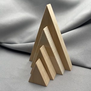 May include: Four wooden triangular prisms of varying sizes are arranged in a row. The largest is at the back, the smallest at the front. The prisms are made of light-coloured wood with a smooth finish. The background is a grey fabric.