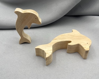 May include: Two wooden dolphin figurines. One dolphin is upright, the other is lying down. Both are made of light-colored wood with a smooth finish. Each dolphin has a small, dark dot for an eye.