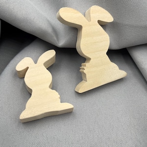 Könnte beinhalten: Zwei Holzausschnitte in Hasenform. Die Hasen sind hell gefärbt und haben eine einfache Silhouette. Die Ohren sind lang und gebogen. Die Hasen sind wahrscheinlich zum Basteln oder Dekorieren gedacht, perfekt für Ostern oder Frühlingsprojekte.
