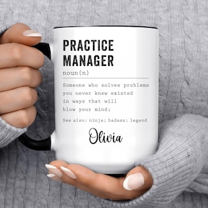 May include: White ceramic mug with a black handle and rim. The mug features the text "PRACTICE MANAGER" above a definition, and the name "Olivia" in cursive. The mug is held by a person.