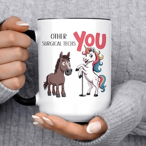 May include: A white ceramic mug with a black handle and rim featuring a cartoon brown horse next to a cartoon unicorn. The text reads OTHER SURGICAL TECHS in black and YOU in large pink letters. The unicorn stands next to a silver pole.