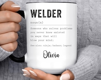May include: White coffee mug with black handle and rim, featuring the word "WELDER" and a definition. The definition reads "Someone who solves problems you never knew existed..." with the name "Olivia" below.