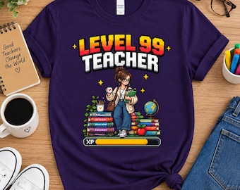 May include: A dark purple t-shirt featuring a pixel art graphic of a teacher standing among stacks of books, a globe, and an apple. The text reads "LEVEL 99 TEACHER" above the character, with an "XP" progress bar displayed at the bottom.