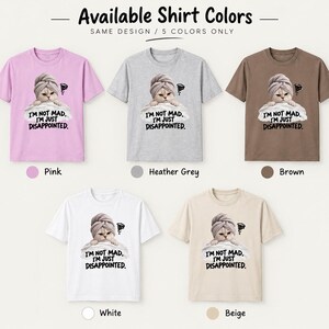 May include: Five short-sleeved t-shirts in pink, heather grey, brown, white, and beige. Each shirt features a graphic of a cat wearing a towel on its head, resting on a pillow, with the text I'M NOT MAD. I'M JUST DISAPPOINTED. printed below.