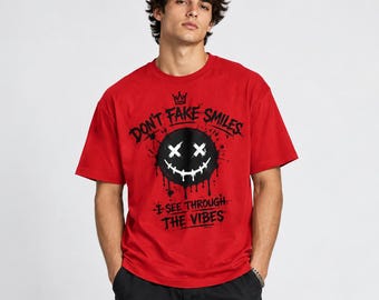 May include: A bright red short-sleeved t-shirt featuring a black graphic of a dripping smiley face with X-shaped eyes and a stitched mouth. The text reads DON'T FAKE SMILES above and I SEE THROUGH THE VIBES below in a distressed black font.