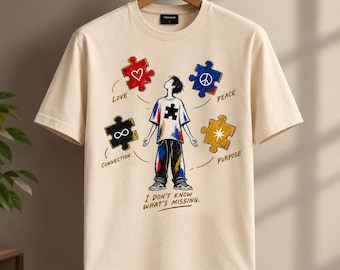 May include: A beige short-sleeve t-shirt featuring a graphic of a person surrounded by four puzzle pieces labelled Love, Peace, Connection, and Purpose. The text I DON'T KNOW WHAT'S MISSING is printed below the figure, which wears a puzzle-themed shirt.