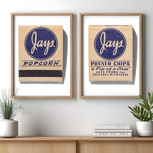 May include: Two framed prints featuring vintage Jays brand packaging. The left print displays a tan matchbook cover with a blue circular logo, the text "jays" and "POPCORN". The right print shows a tan package with "jays", "POTATO CHIPS", "a Pip of a Chip", and "JAYS FOODS, Inc. CHICAGO MILWAUKEE".