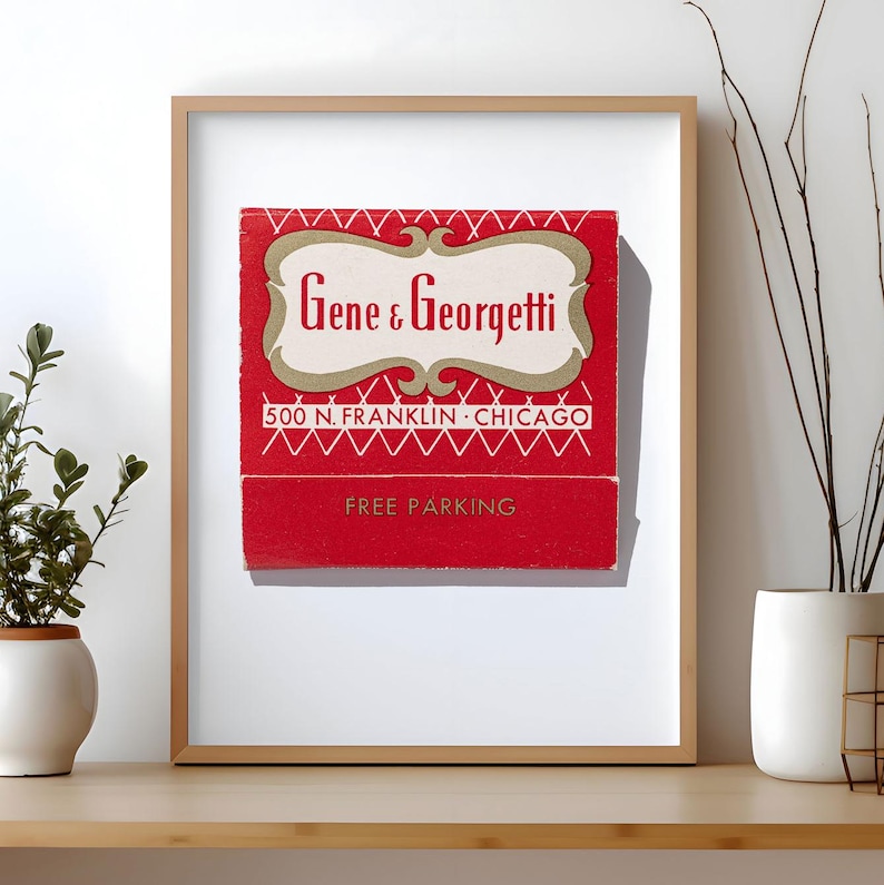 May include: A framed print featuring a vintage red matchbook cover with the text Gene & Georgetti, 500 N. FRANKLIN CHICAGO, and FREE PARKING. The design includes a cream-colored decorative border and white geometric line patterns on a red background.