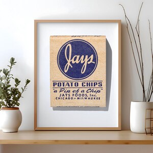 May include: A framed print featuring a vintage-style tan matchbox with a blue circular logo that reads "jays" in script. Below the logo, the text reads "POTATO CHIPS", "a Pip of a Chip", and "JAYS FOODS, Inc. CHICAGO &bull; MILWAUKEE" in blue lettering.