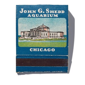 Peut inclure: Une couverture de bo&icirc;te d'allumettes vintage repr&eacute;sentant une illustration bleue et blanche de l'aquarium John G. Shedd &agrave; Chicago. Le texte "John G. Shedd Aquarium" et "Chicago" est imprim&eacute; en blanc sur fond bleu.