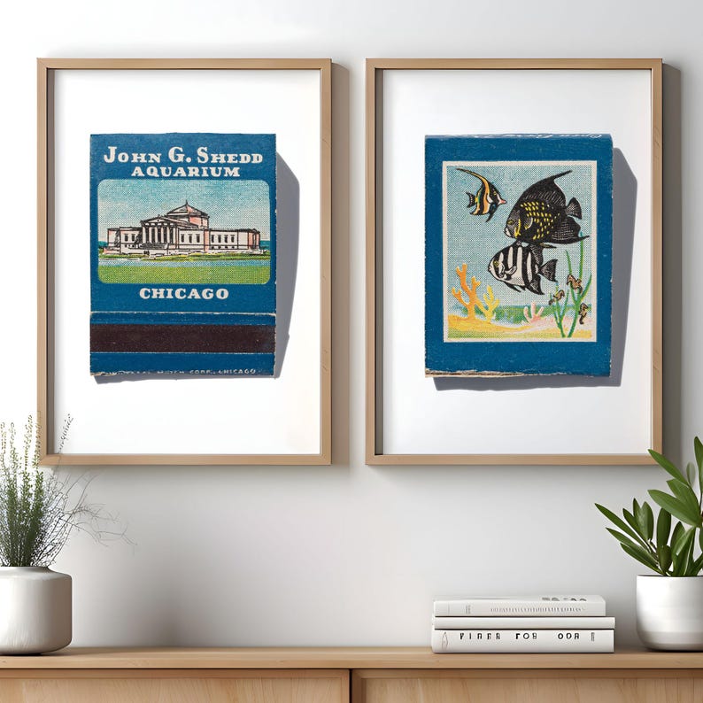 Peut inclure: Deux impressions encadr&eacute;es de couvertures de bo&icirc;tes d'allumettes vintage. L'impression de gauche pr&eacute;sente une couverture de bo&icirc;te d'allumettes bleue avec le texte "John G. Shedd Aquarium Chicago" et un dessin du b&acirc;timent de l'aquarium. L'impression de droite pr&eacute;sente une couverture de bo&icirc;te d'allumettes bleue avec un dessin de trois poissons noirs et blancs dans un r&eacute;cif corallien.