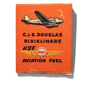 May include: Orange matchbox with a black and white illustration of an airplane flying. The text on the matchbox reads "C. & S. DOUGLAS DIXIELINERS USE SHELL AVIATION FUEL Made in U.S.A. THE DIAMOND MATCH CO. N.Y.C."