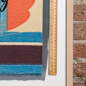 May include: A close-up of a vintage poster with a red heart, blue and brown stripes, and the text "Going to the Big City". The poster is framed and next to a ruler.