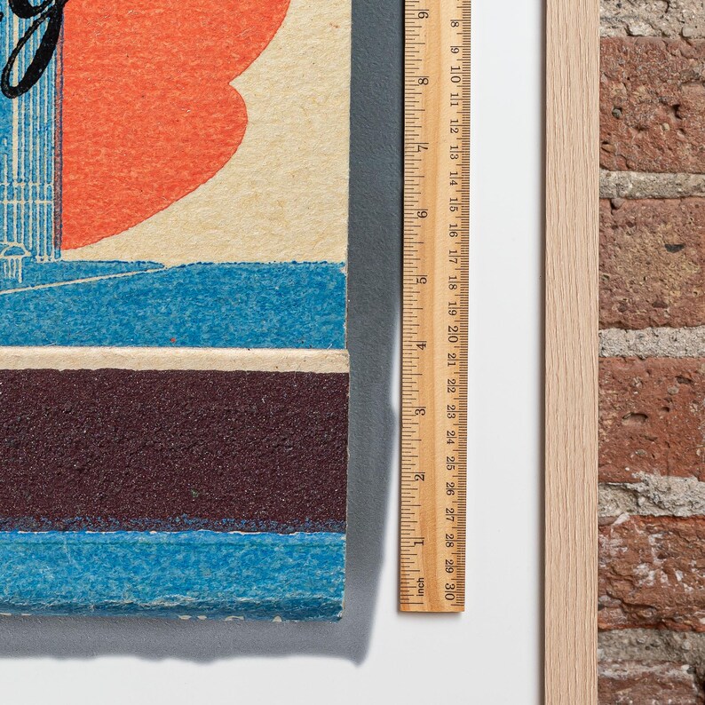 May include: A close-up of a vintage poster with a red heart, blue and brown stripes, and the text "Going to the Big City". The poster is framed and next to a ruler.