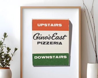 May include: A framed print featuring a rectangular graphic with an orange top section labelled UPSTAIRS, a white middle section with the black text Gino's East PIZZERIA, and a green bottom section labelled DOWNSTAIRS in white capital letters.