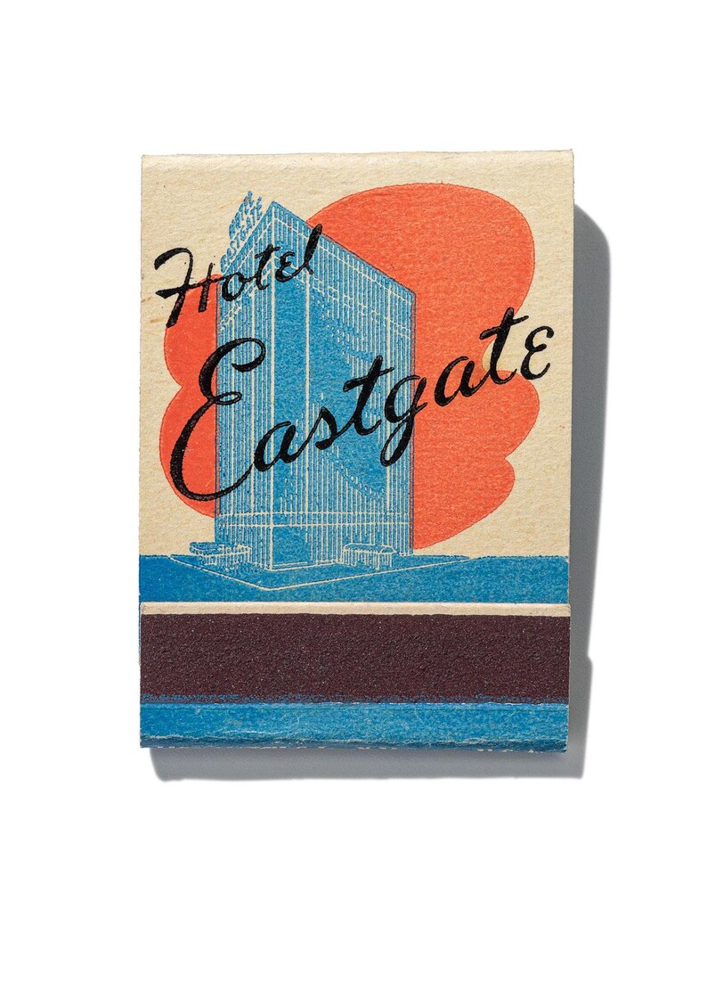 May include: Vintage matchbook cover featuring a blue and white illustration of a skyscraper with the text "Hotel Eastgate" in black cursive lettering on a cream background with a red sunburst.