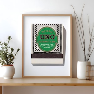 May include: A framed print featuring a vintage matchbook cover for Pizzeria Uno Restaurant & Bar. The design includes a green oval with black text reading Pizzeria Uno Restaurant & Bar, Established 1943, Cor. Wabash & Ohio, Chicago, on a grid.