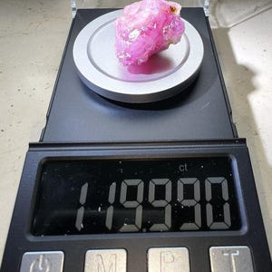 May include: A pink ruby gemstone weighing 1.9900 carats on a digital scale.