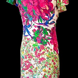 May include: A white dress with a vibrant floral print featuring large magenta and pink flowers, green leaves, and blue accents. The dress has a fitted bodice and a flowing skirt, with a contrasting floral pattern on the sleeves.