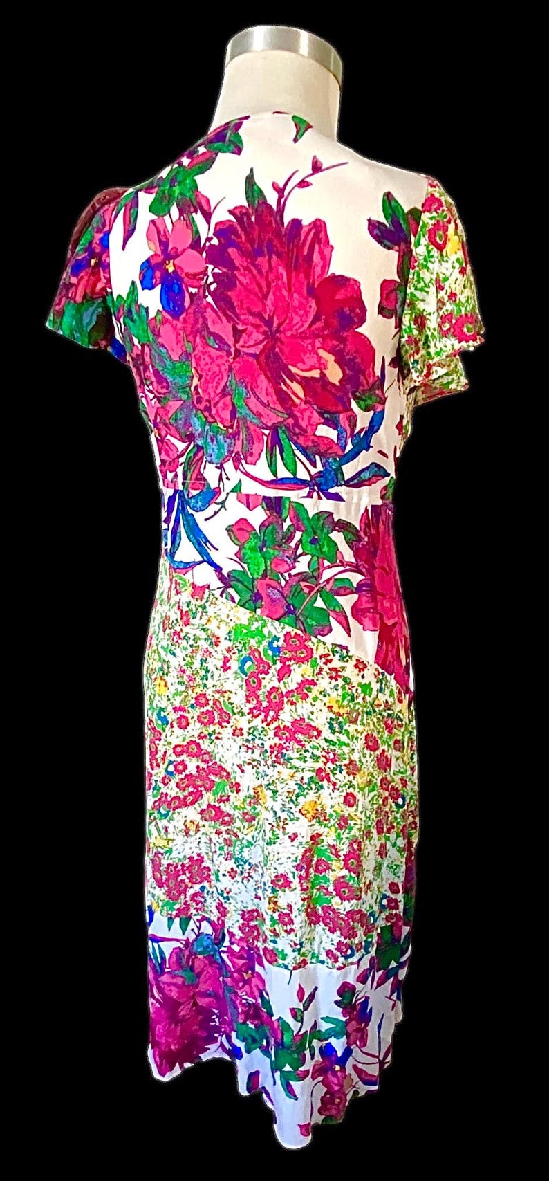 May include: A white dress with a vibrant floral print featuring large magenta and pink flowers, green leaves, and blue accents. The dress has a fitted bodice and a flowing skirt, with a contrasting floral pattern on the sleeves.