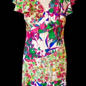 May include: A floral print dress with a V-neck and flutter sleeves. The dress features a white background with vibrant pink, green, blue, and yellow floral patterns. The dress is displayed on a mannequin.