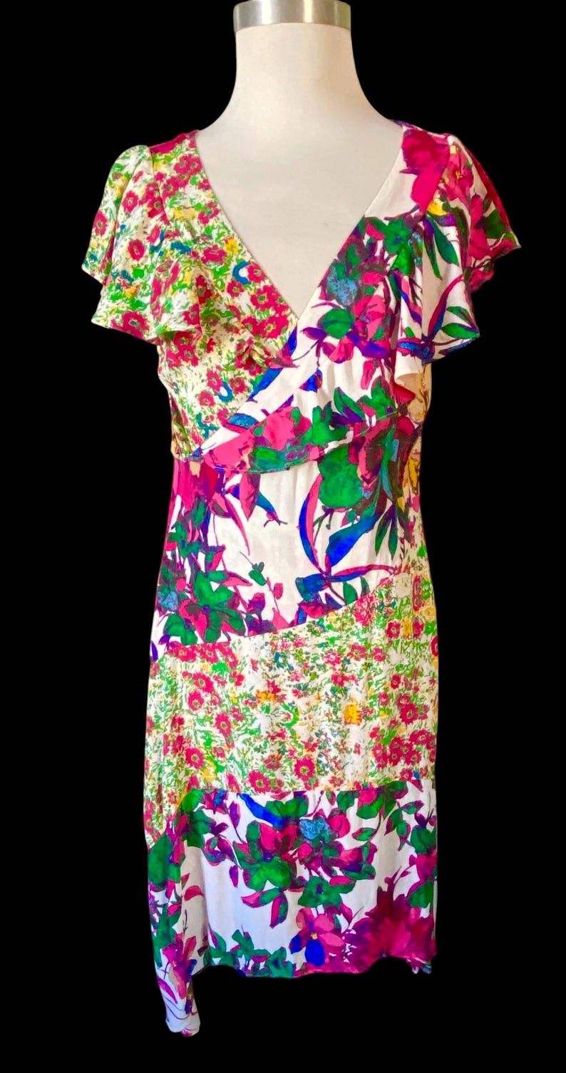 May include: A floral print dress with a V-neck and flutter sleeves. The dress features a white background with vibrant pink, green, blue, and yellow floral patterns. The dress is displayed on a mannequin.