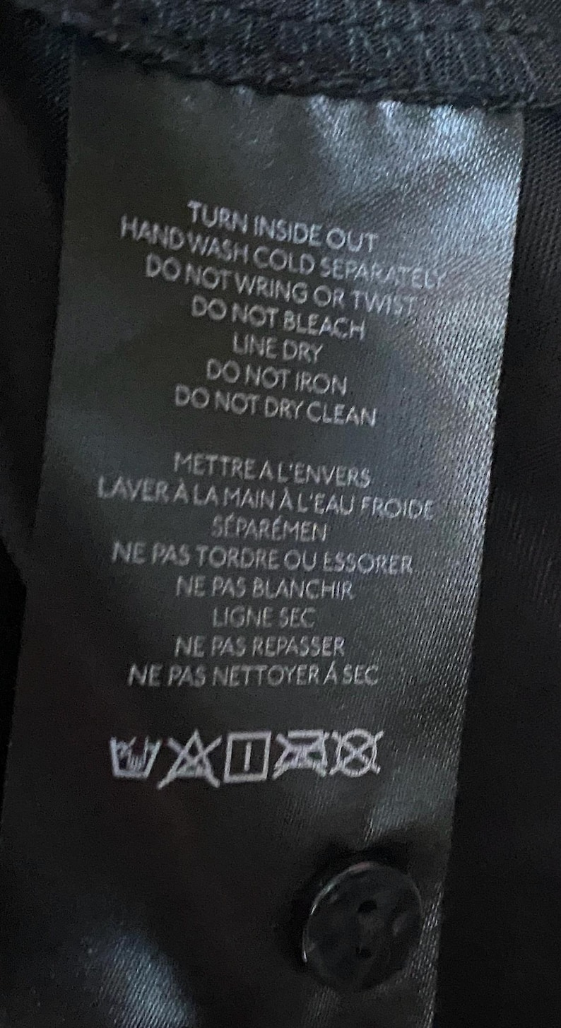 May include: Black care label with white text detailing washing instructions. The text reads "Turn inside out, hand wash cold separately, do not wring or twist, do not bleach, line dry, do not iron, do not dry clean". The label also includes French instructions and washing symbols.