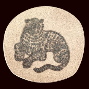 May include: A round ceramic plate with a speckled beige surface featuring a dark gray embossed illustration of a leopard in a resting position. The leopard is depicted with detailed spots covering its body, head, and long tail, centered on the plate.