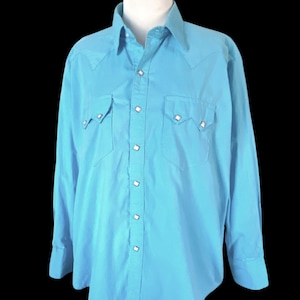 May include: A turquoise Western-style shirt with long sleeves. The shirt features two chest pockets, decorative stitching on the shoulders and pockets, and pearl snap closures down the front and on the cuffs. The shirt is displayed on a white mannequin.