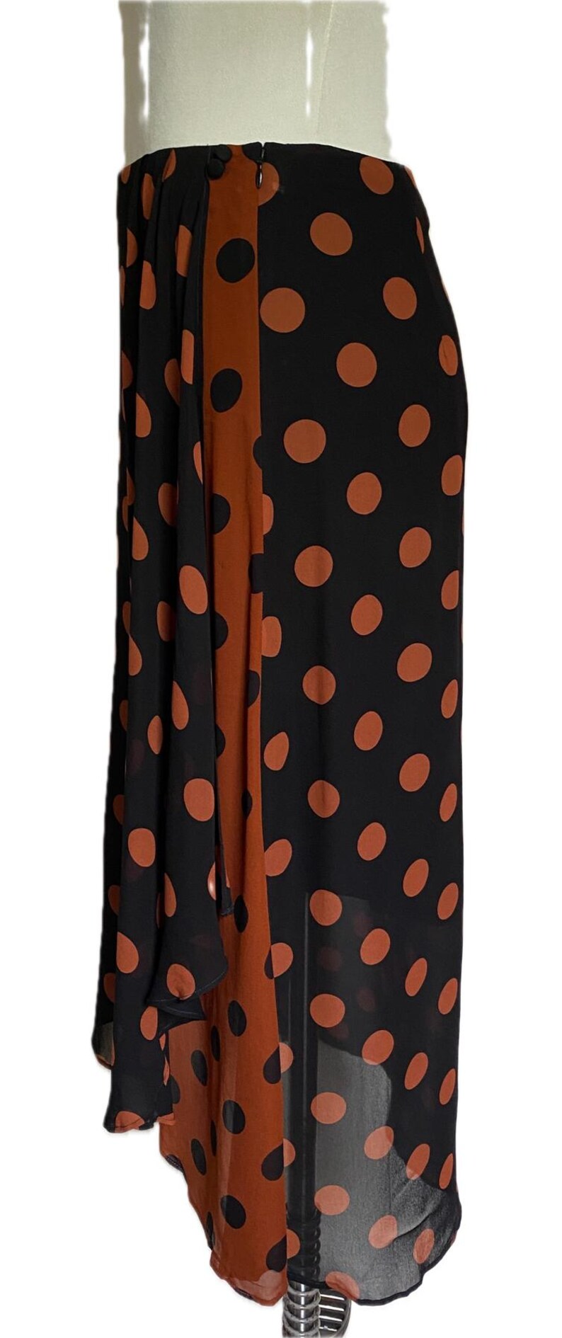 以下が含まれることがあります： 黒いスカートに、大きな錆色の水玉模様。 垂直な錆色のパネルが側面を走っています。 スカートは、流れるような軽い生地で作られています。 スカートはマネキンに展示されています。
