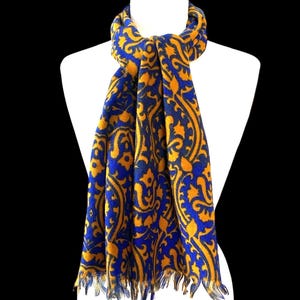 May include: A blue and gold scarf with an intricate paisley pattern. The scarf is draped over a white mannequin, showcasing its design and fringed edges. The color scheme is a striking combination of royal blue and golden yellow.