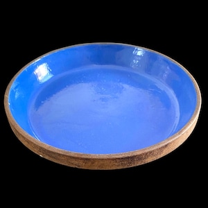 May include: A round ceramic dish with a vibrant blue interior and a textured, brown rim. The dish has a shallow depth and a glossy finish, perfect for serving or display. The contrast between the blue and brown creates a striking visual appeal.
