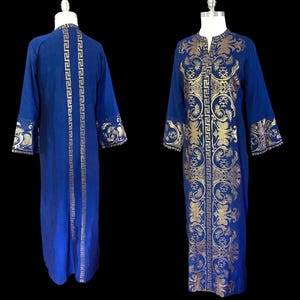 May include: A long-sleeved, floor-length blue kaftan dress featuring a prominent gold metallic print. The design includes a vertical Greek key pattern along the center front and back, complemented by intricate floral motifs on the chest and cuffs.