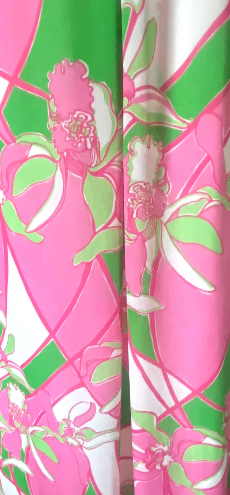 Op de afbeelding: Close-up van een stof met een levendig bloemenpatroon. Het ontwerp toont grote roze bloemen met groene en witte accenten tegen een groen-witte geometrische achtergrond. De algehele esthetiek is helder en kleurrijk.