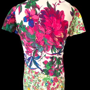 May include: A vintage dress featuring a vibrant floral print. The dress has a white background with large pink, blue, and green flowers on the bodice. The sleeves and lower portion of the dress have smaller floral patterns.