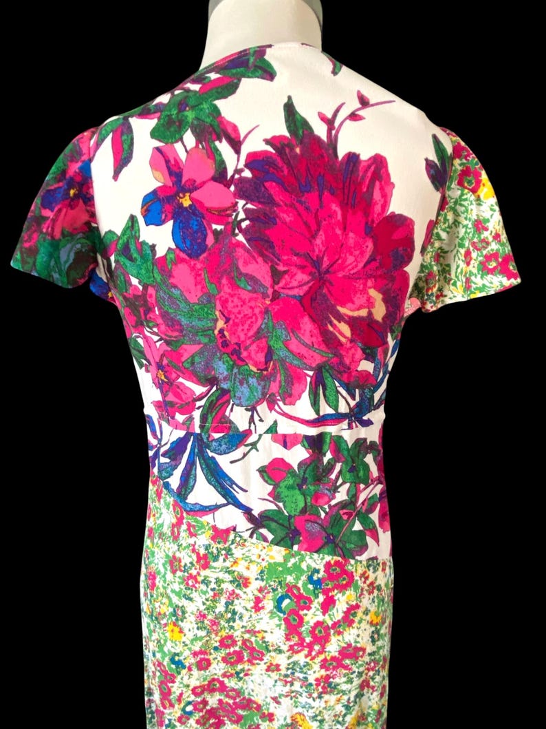 May include: A vintage dress featuring a vibrant floral print. The dress has a white background with large pink, blue, and green flowers on the bodice. The sleeves and lower portion of the dress have smaller floral patterns.