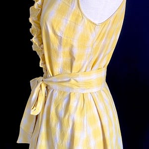 K&ouml;nnte beinhalten: Ein gelbes und wei&szlig;es kariertes, &auml;rmelloses Kleid mit R&uuml;schenkragen und einer Schleife in der Taille.