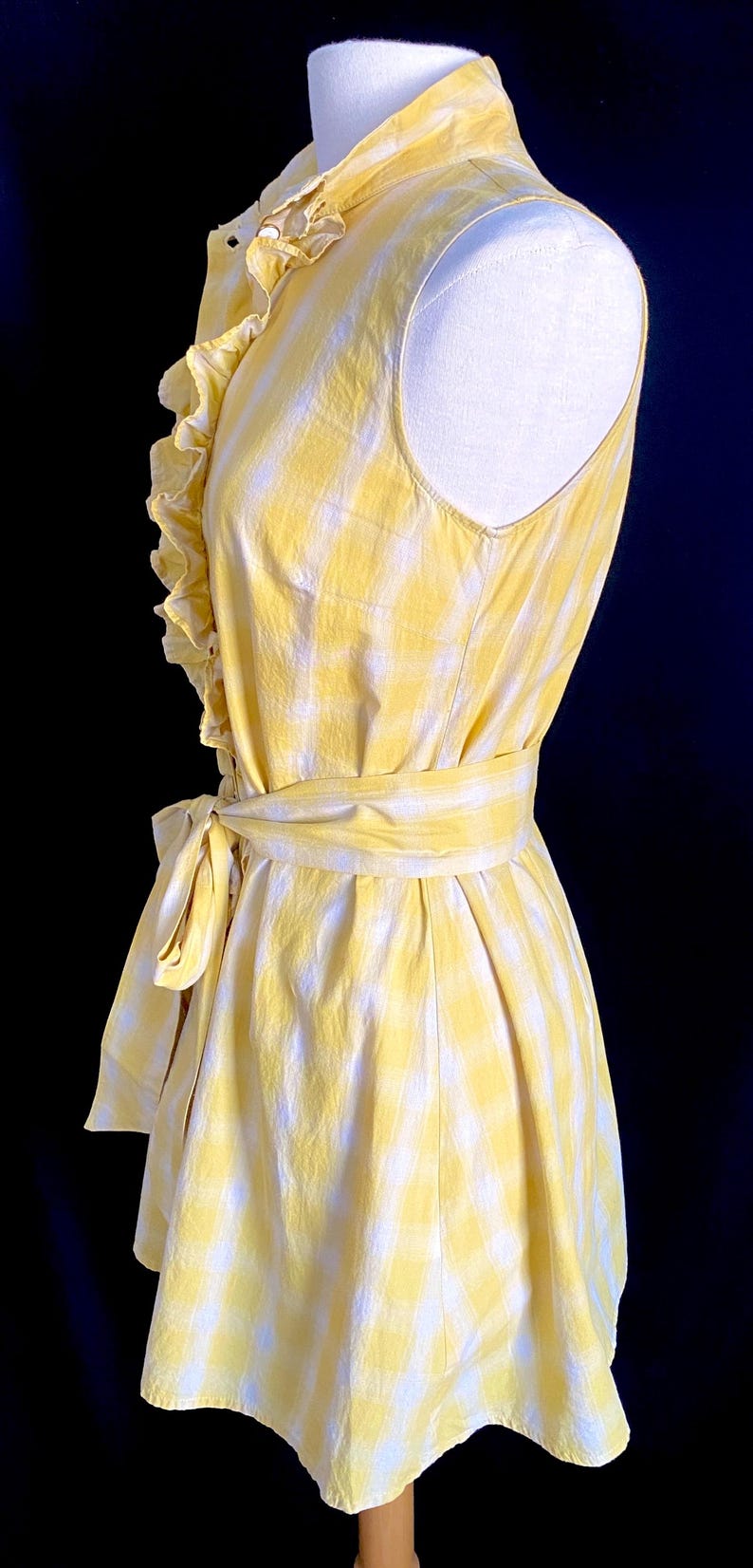 K&ouml;nnte beinhalten: Ein gelbes und wei&szlig;es kariertes, &auml;rmelloses Kleid mit R&uuml;schenkragen und einer Schleife in der Taille.