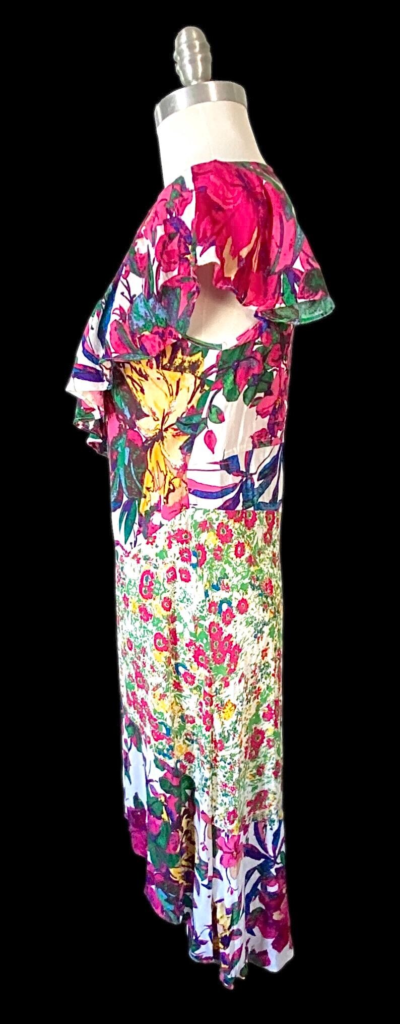 May include: A floral print dress with a white base, featuring large pink, yellow, and blue flowers. The dress has a ruffled neckline and a flowing, floor-length design, perfect for a summer event.