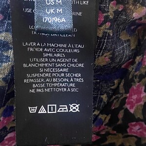 May include: A black clothing tag with white text, including size information: US M, UK M, and 170/96A. The tag also features washing instructions in French, along with care symbols for machine washing at 30 degrees.