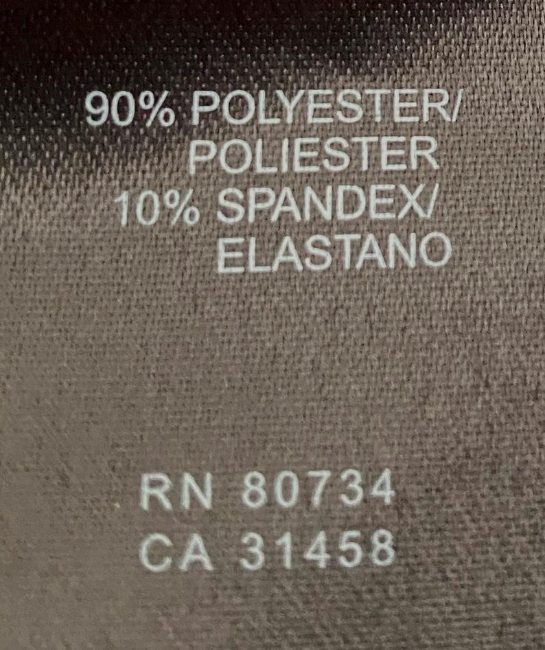 May include: A brown fabric tag with white text. The tag states "90% Polyester/Poliester 10% Spandex/Elastano" and "RN 80734 CA 31458".