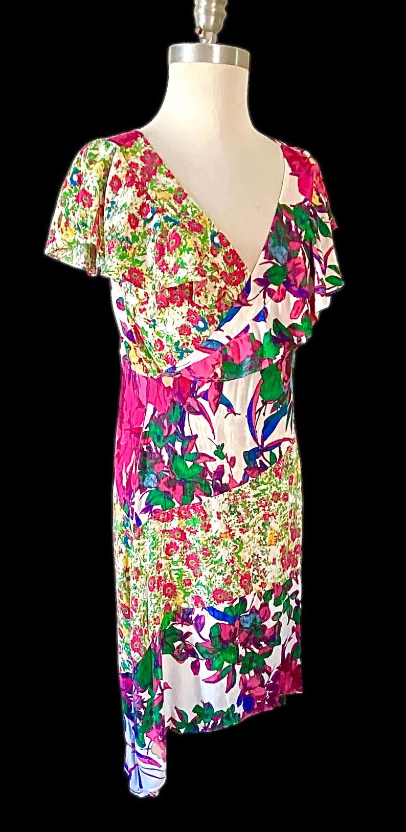 May include: A floral print dress with a V-neckline and flutter sleeves. The dress features a mix of pink, green, and blue floral patterns on a white background. The dress is displayed on a mannequin.