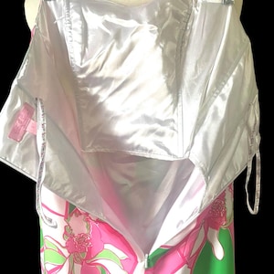 Op de afbeelding: Een strapless jurk met een levendig bloemenpatroon in roze, groen en wit, hangend aan een hanger. De jurk heeft een witte satijnen voering en een ritssluiting. De jurk wordt gepresenteerd tegen een zwarte achtergrond.