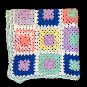 May include: A colorful, handmade crochet blanket featuring a patchwork design of squares in various pastel colors, including pink, blue, yellow, and green. The blanket has a white border and a scalloped edge.