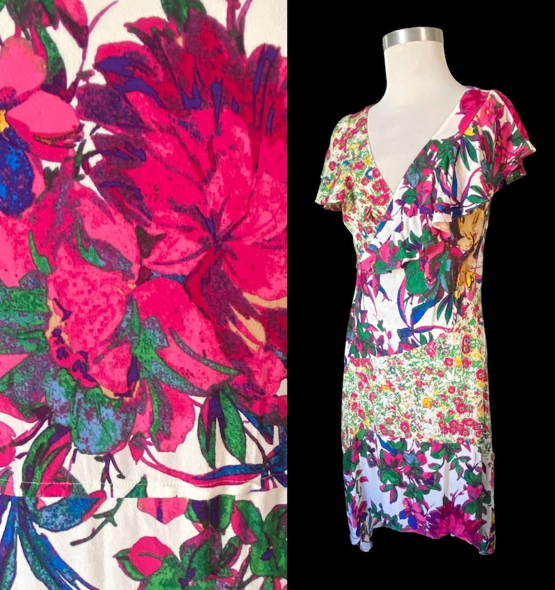 May include: A floral print dress with a V-neck and short sleeves. The dress features a vibrant pattern of pink, green, blue, and yellow flowers on a white background. The dress is displayed on a mannequin against a black backdrop.