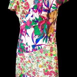 May include: A white, floral-print dress with a V-neckline and ruffled sleeves. The dress features a patchwork design with pink, green, blue, and yellow flowers. The dress is sleeveless and has a flowing skirt.