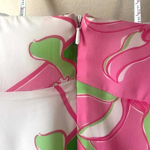 Op de afbeelding: Close-up van een kledingstuk met een witte rits. De stof heeft een bloemenpatroon in roze en groen op een witte achtergrond. Een meetlint met tekst is zichtbaar.