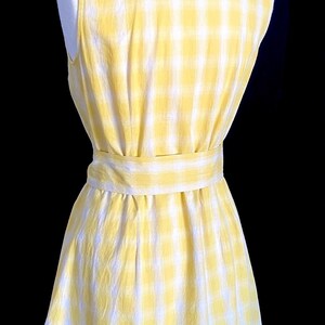 K&ouml;nnte beinhalten: Ein &auml;rmelloses gelbes und wei&szlig;es Gingham-Kleid mit einem Bindeg&uuml;rtel.
